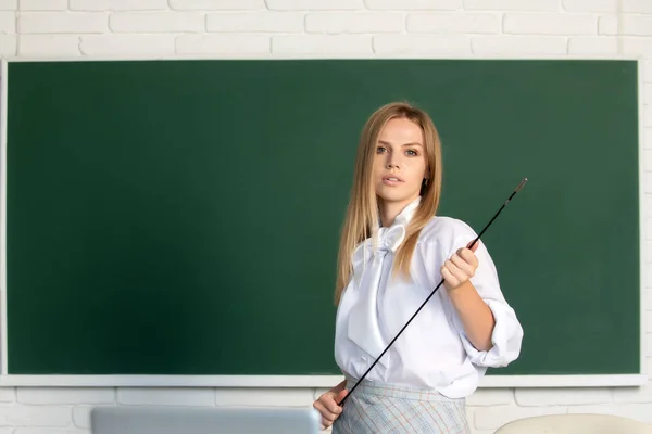 Jonge serieuze leraar die wijst op de les. Schattige jonge vrouw met pointer onderwijs in de buurt van schoolbord. — Stockfoto