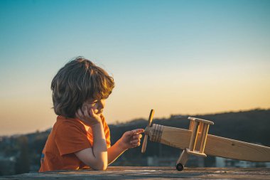 Mavi gökyüzü arka planında oyuncak uçakla oynayan mutlu çocuk. Güneşli bir yaz gününde yürüyen sevimli bir çocuk. Çocuklar seyahat hayali kurar. Tatlı çocuk suratı. Kırsalda yaz.