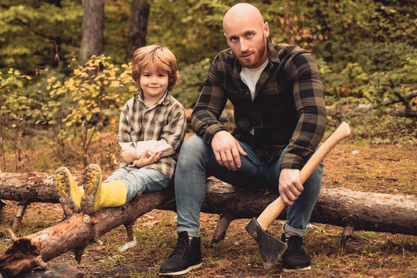 Отец и сын в походе приключения в лесу. Симпатичный ребенок с отцом на улице. Красивый молодой отец и сын рубят дрова топором. — стоковое фото