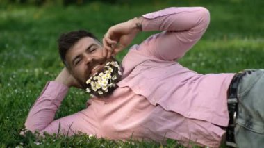 Hippi sakallı papatya çayıyla çimlerin üzerinde yatıyor. Mutlu yüzlü sakallı adam baharın tadını çıkarıyor. Sakallı hippi mutlu görünüyor..