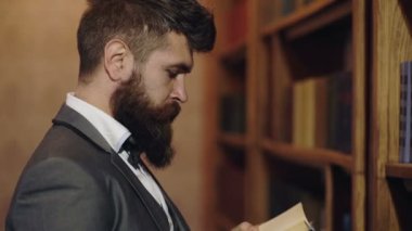 Kütüphanede olgun bir adam ve okumayı seviyor. Takım elbiseli sakallı adam memnun görünüyor. Keyif ve rahatlama, hobi konsepti. Adam kütüphanede kitap seçiyor..