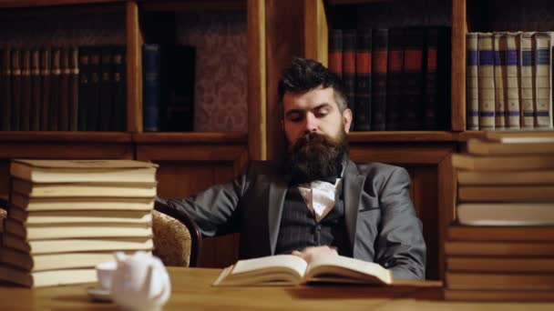 Bearded man in library with books on background. Middle age man reading books at home library. — Stock Video