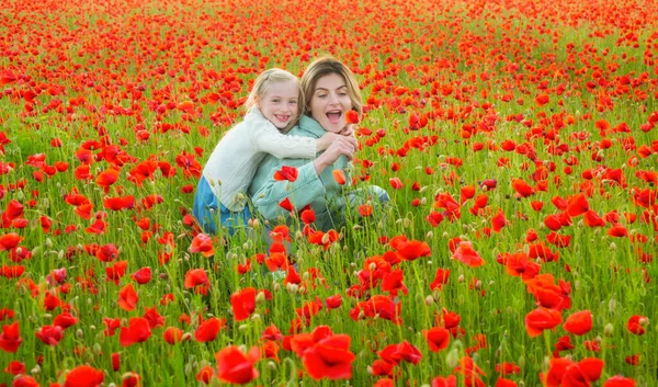 Hermosa madre e hija en el campo de flores de amapola de primavera. Mamá sostiene a su hija en el paseo a cuestas del prado floreciente. Feliz maternidad.. —  Fotos de Stock