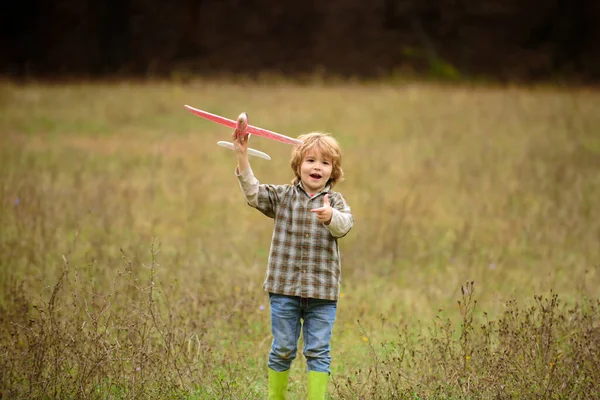 Miúdo a divertir-se com aviões de brincar no terreno. Menino com avião de madeira, menino quer se tornar piloto e astronauta. Brincadeira de criança feliz com avião de brinquedo. Crianças piloto sonhos de voar no campo. — Fotografia de Stock