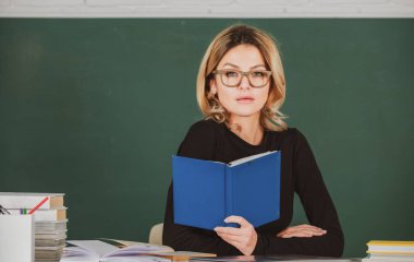 Kara tahtanın yanında gözlüklü şehvetli öğrenci kadın. Seksi kız masadaki tahtaya oturur. Üniversitede çekici bir bayan öğretmen. Konsept çalış.