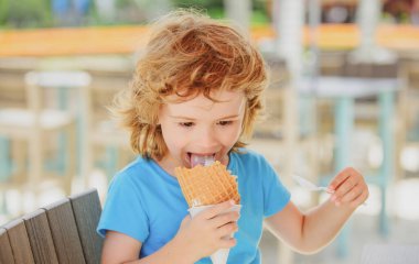 Tatlı çocuk waffle külahında büyük dondurmayı yalıyor. Çocuklar kafede dondurma yiyorlar..