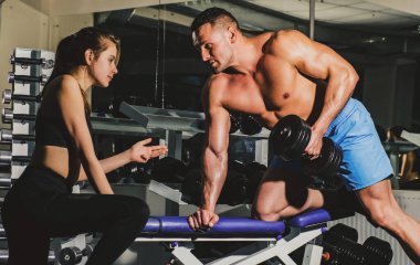 Mutlu fitness çifti. Spor salonunda ağır halterlerle çalışan bir kadına kişisel antrenör yardım ediyor. Sporcu konsepti. Spor kadını. Çıplak gövdeli sportif bir erkek. Egzersizler. Güçlü atletik vücut.