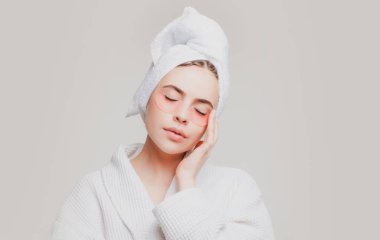 Göz bandı takan bir kadın. Kafasında havluyla portre kızı yakın plan. Şehvetli kız göz torbasını küçültür. Yüz kolajeni cilt estetiği. Nemlendirici cilt. Anti-yorgunluk maskesi takılıyor.