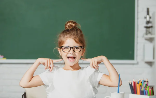 Αστεία σχολική φάτσα με γυαλιά. Ένα κοριτσάκι στο σχολείο ζωγραφίζει με μπογιές. Δημιουργικότητα παιδιών καλλιτεχνών. — Φωτογραφία Αρχείου