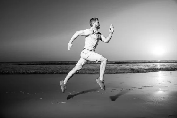 Een man die bij zonsondergang op het strand rent. Een jogger op de vlucht. Dynamisch springen. Sportsprong. — Stockfoto