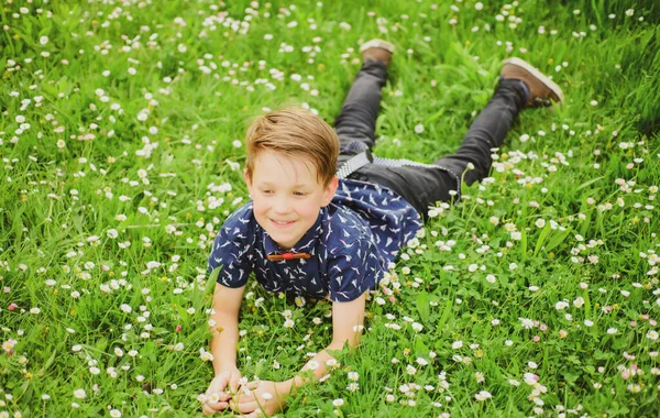 Ragazzo sorridente sdraiato sull'erba. Bambino carino godendo sul prato campo fiore e sognando. — Foto Stock