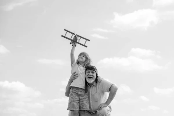 Dziecko chłopiec i dziadek z samolotem zabawki nad błękitnym niebem i chmury tła. Mężczyźni pokolenie dziadek i wnuk bawią się na świeżym powietrzu. — Zdjęcie stockowe