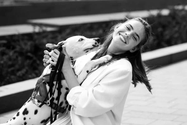 Foto de estilo callejero de mujer excitada elegante paseando con perro. Perro lamiendo y besando divertido lanzamiento chica. — Foto de Stock