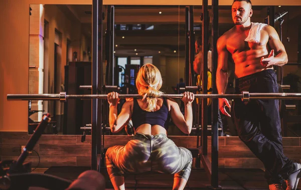 Entrenamiento de pareja deportiva joven con barra de pesas en el gimnasio. Entrenador muscular hombre entrenamiento mujer Entrenador personal instructor de fitness. — Foto de Stock