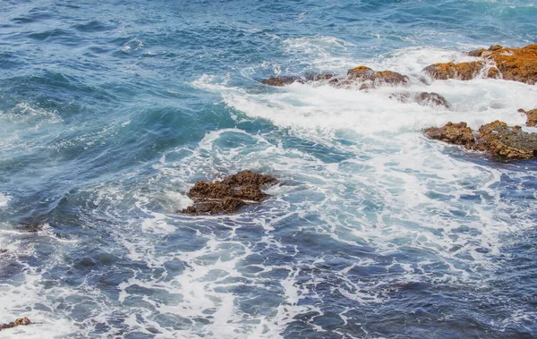 Blaues Meer und Felsen stürmen. Wellen sprühen über Felsen. Felsige Meeresküste. — Stockfoto