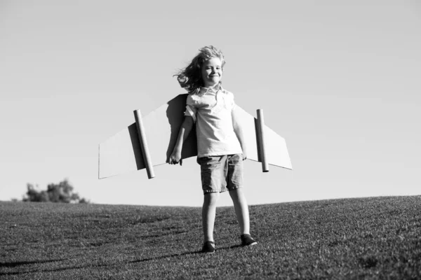 Drôle de garçon avec des ailes d'avion en carton jouet voler. Concept de liberté de démarrage. Enfant portant un costume d'aviateur extérieur. Imagine peu de rêves de pilote de voler. — Photo