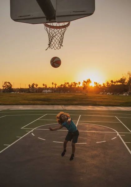 Glücklicher kleiner Junge, der Basketball auf dem Spielplatz spielt. Niedliche kleine Junge Kind springen mit Korbball für Schuss auf Sonnenuntergang. — Stockfoto