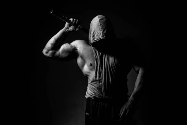 Hombre musculoso peligroso en la máscara con bate de béisbol listo para la pelea. Un agresivo encapuchado sostiene un bate de béisbol sobre negro. — Foto de Stock