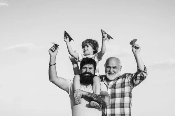 公園で楽しんでいる息子と孫と祖父。夏の空を背景にしたおもちゃの紙飛行機で遊ぶ幸せな子供。子供は幸せだ。家族で楽しむ. — ストック写真
