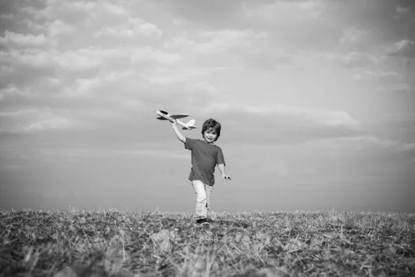 子供の頃の思い出-牧草地の美しい空。子供の頃の夢の想像の概念。アクティブな子供の演奏。楽しさと笑顔を持つ牧草地の上におもちゃの飛行機で遊ぶ子供. — ストック写真