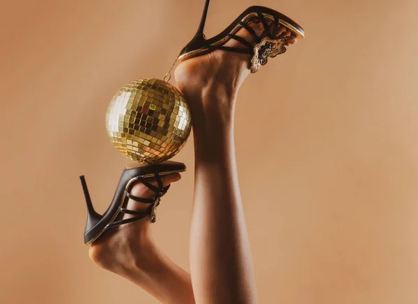 Seksi kadın bacakları. Disko partisi etkinliği. Altın disko topu olan yüksek topuklu bir kadın. Arkaplan kutlanıyor. — Stok fotoğraf