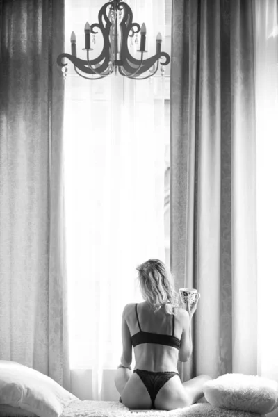 Zrelaksowana młoda zmysłowa modelka z filiżankami kawy w łóżku w domu. Widok z tyłu młody pasuje zdrowe kobiety w sypialni. Dzień dobry, piję kawę. — Zdjęcie stockowe
