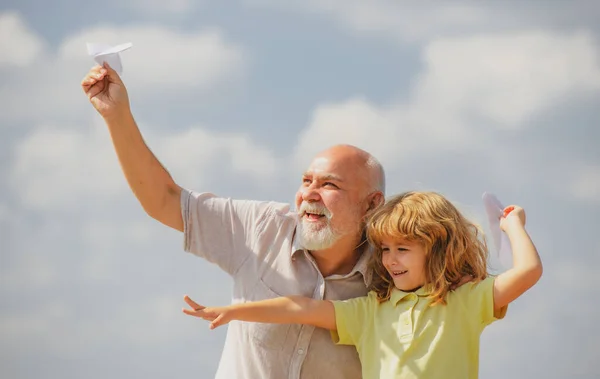 Menino e avô com avião de papel sobre céu azul e nuvens. Homens geração avô e neto. Parente idoso com filho. — Fotografia de Stock