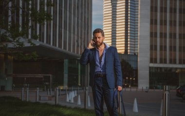 Arka planda şehir manzarası olan modern bir iş adamı telefonda konuşuyor..