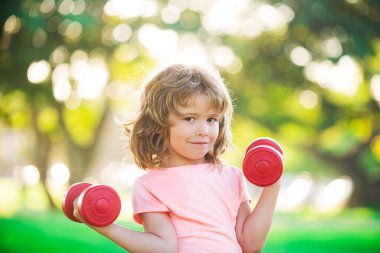 Fitness çocuğu. Parkda dambılı küçük bir çocuğun portresi. Jimnastik. Çocuk sporcusu, çocukluk aktivitesi. Çocuklar spor ve spor.