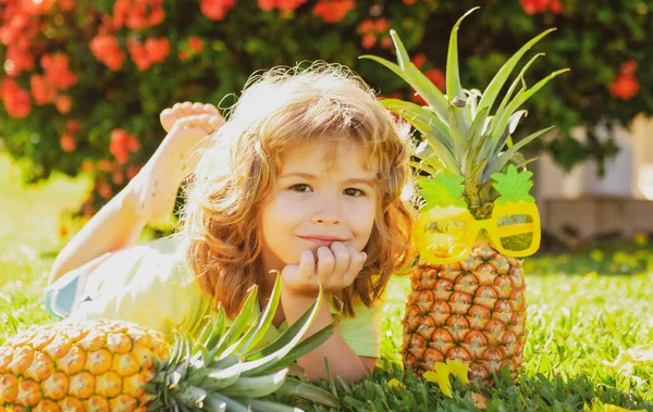 Jovem garoto engraçado segurando abacaxi e sorrindo no quintal. Um miúdo com ananás. Crianças fruta de verão. — Fotografia de Stock