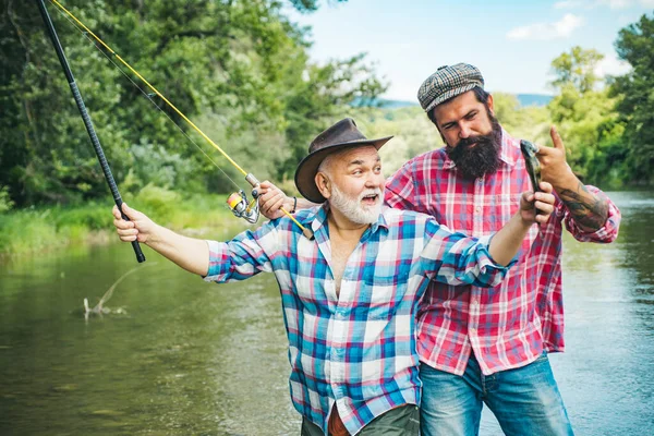 快乐兴奋的男人朋友。一个快乐的老人钓鱼的画像。祖父和儿子是渔夫。年轻人和老人在河里或湖中钓菠萝. — 图库照片