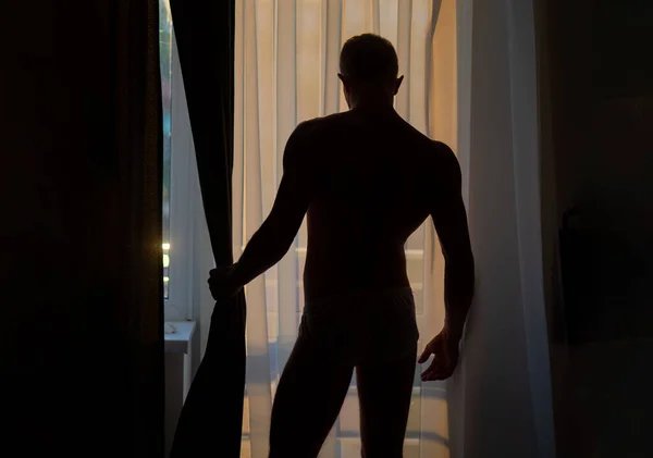 Seksowna gejowska sylwetka. Seksowny nagi muskularny mężczyzna przy oknie. Człowiek bez koszuli pokryty cieniem z okna. — Zdjęcie stockowe