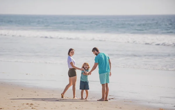 快乐的年轻家庭在夏天的海滩上奔跑和跳跃。和父母在户外的孩子童年和养育概念. — 图库照片