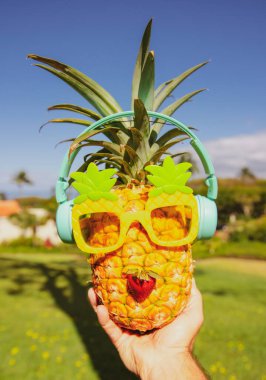 Yaz tropik ananas arka planı. Ananas güneş gözlüklü, mavi gökyüzü arka planında bir palmiye ağacının altında. Plajda kokteyl partisi, dinlenme, rahatlama ve yaz konsepti..