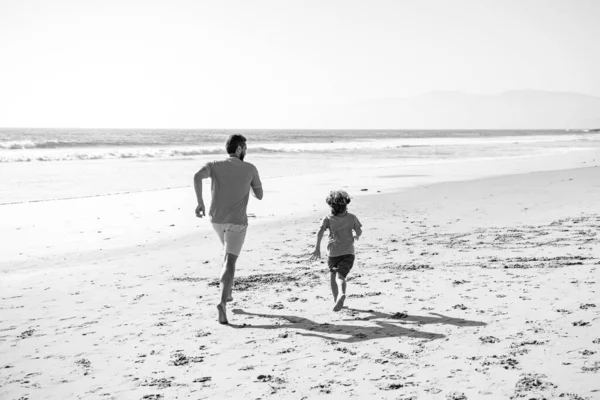 Padre e hijo corriendo en el mar. Papá y su hijo se divierten al aire libre. Viajes en familia, vacaciones, padres concepto de día. —  Fotos de Stock