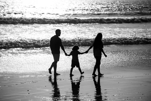 Silhouette di padre, madre e figlio figlio che si tiene per mano e cammina sulla spiaggia. Stile di vita Sctive fanily, genitori con bambini in vacanza estiva. — Foto Stock