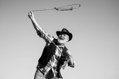 Vahşi batı kovboyu rodeoda. Kementle bağlanmış batı emeklisi. Sakallı, kahverengi ceketli, şapkalı, at ya da inek yakalayan adam..