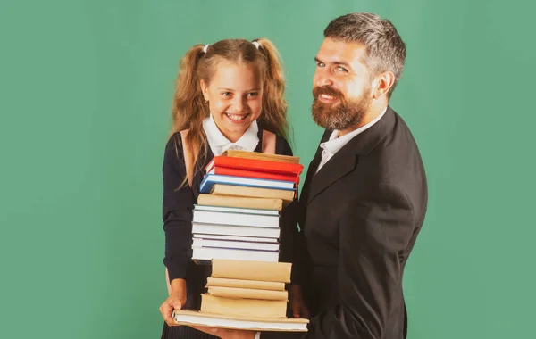 Vater führt seine Schülerin zur Schule. Porträt eines modernen Familienvaters und kleiner Mädchen isoliert auf einer grünen Tafel. Kleines Mädchen mit einem Stapel Bücher. Schwer zu studieren. — Stockfoto