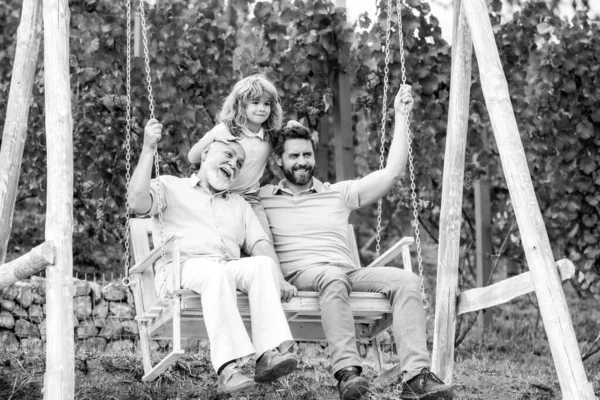Ενθουσιασμένος παππούς και γιος παίζουν έξω, κάθονται στην κούνια. Ευτυχισμένη οικογένεια ανδρών. Τρεις άνδρες γενιά. — Φωτογραφία Αρχείου