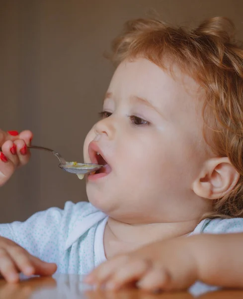 Moeder voedt baby met lepel. Het geven van fruitsaus aan kleine jongen. — Stockfoto