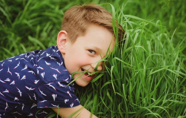 Leende pojke med gräs bakgrund. Söt unge som njuter på fältet. Enighet med naturen. — Stockfoto