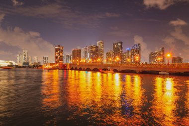Miami şehri. Alacakaranlıkta deniz üzerinde gökdelenlerle Miami gökyüzü manzarası. Sanset 'te gece.