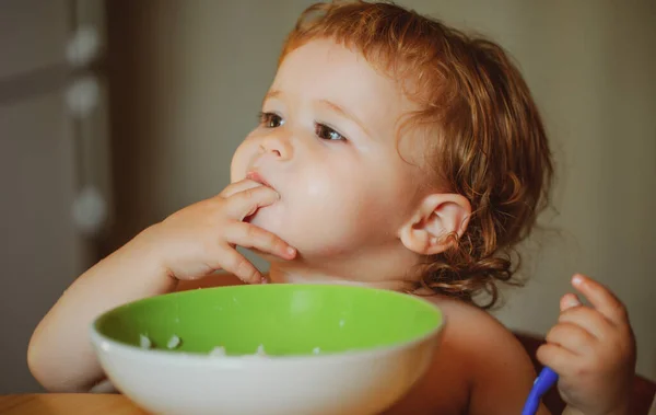 Um bebezinho engraçado na cozinha a comer com os dedos do prato. Conceito de nutrição infantil. — Fotografia de Stock