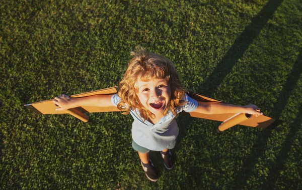 おもちゃのジェットパックで遊ぶ素晴らしい子供。興奮した子供のパイロット宇宙飛行士や宇宙飛行士の夢。航空機の少年は段ボールの翼で飛んでいます。少年は飛ぶ夢を見る。屋外で遊ぶ無料の子供. — ストック写真