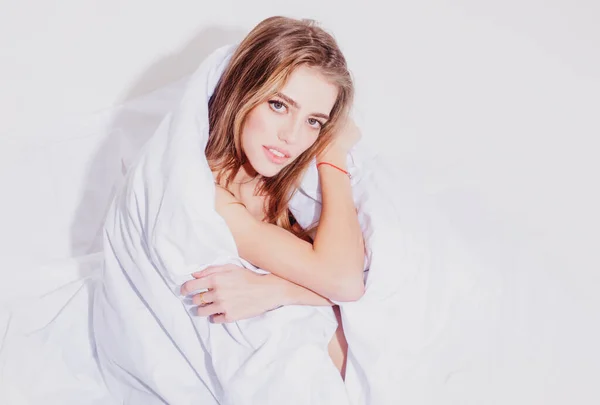 Mujer sexy con cara hermosa está sentado en la cama, envuelto en una manta suave. —  Fotos de Stock