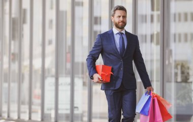 Alışveriş torbaları tutan ve alışveriş mağazasında yürüyen bir iş adamı. Alışveriş ve ödeme. Alışverişkolik alışveriş kavramı.