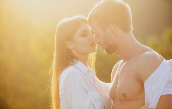 Portrait of lovely couple in love at sunset. Young sensual girlfriend glad to passionate kiss from her boyfriend. Handsome young man embraces his woman and kisses.