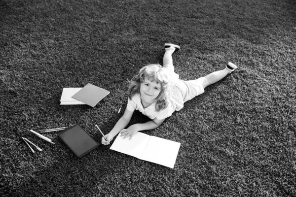 Mooi kind jongen schrijven op notebook op gras achtergrond. Kinderen die boeken lezen in het park. Concept van kinderen leren, studeren, school en aandacht. — Stockfoto