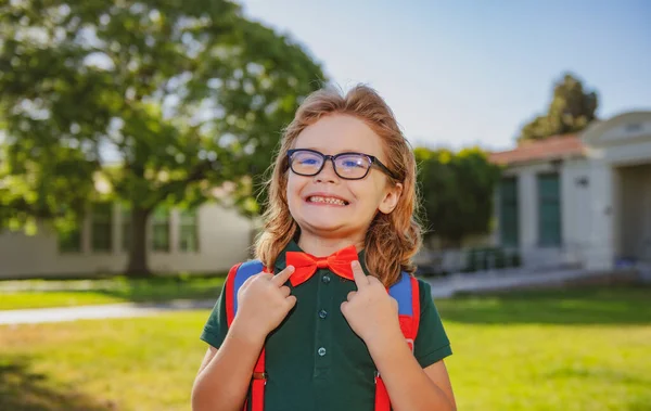 Σχολική παιδική ιδέα. Χαριτωμένο κατάπληκτος μαθητής, παιδί σε σχολική στολή με σακίδιο εξωτερική. Πορτραίτο του σπασίκλα. — Φωτογραφία Αρχείου