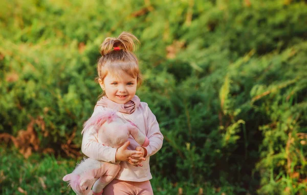 Liten flicka med leksak leker i naturen på det gröna gräset. Ungarna leker. Baby och sommar soligt väder. — Stockfoto
